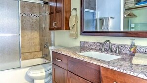 A bathroom with a shower, toilet, vanity with a sink, and a large mirror. - Heavenly Kauai Destinations Hale Moi Side B by Hideaways Beach (Princeville)