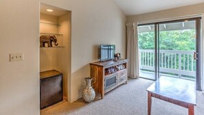 A room with a wooden cabinet, a small TV, a vase, and a balcony with a view of greenery. - Heavenly Kauai Destinations Hale Moi Side B by Hideaways Beach (Princeville)
