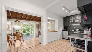 A spacious kitchen with white cabinetry, a wooden dining area, and a large window overlooking greenery.