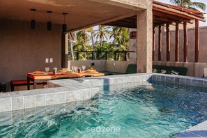 Una piscina con bordes de azulejos, una mesa de madera con sillas y vistas a palmeras.