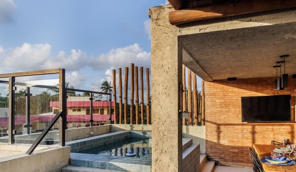 Un área de piscina moderna al aire libre con cerramiento de vidrio, pared de ladrillo y valla de madera.