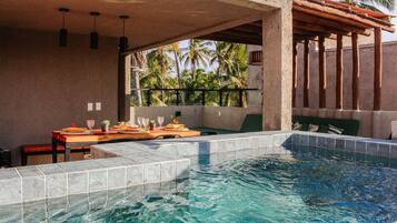 A swimming pool with tiled edges, a wooden table with chairs, and a view of palm trees.