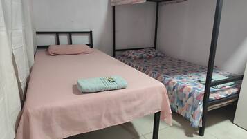 A single bed with a pink bedspread, a smaller bed with a patterned bedspread, and a bunk bed with a checkered canopy.