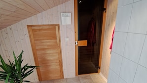 A room with wooden walls, a tiled floor, a wooden door, a potted plant, and a tiled wall with a light fixture.