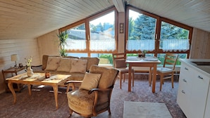 A cozy room with a wooden ceiling, a sofa set, a dining table, and a kitchen area.