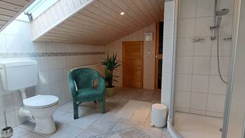 Een badkamer met een douche, toilet en een groene stoel.