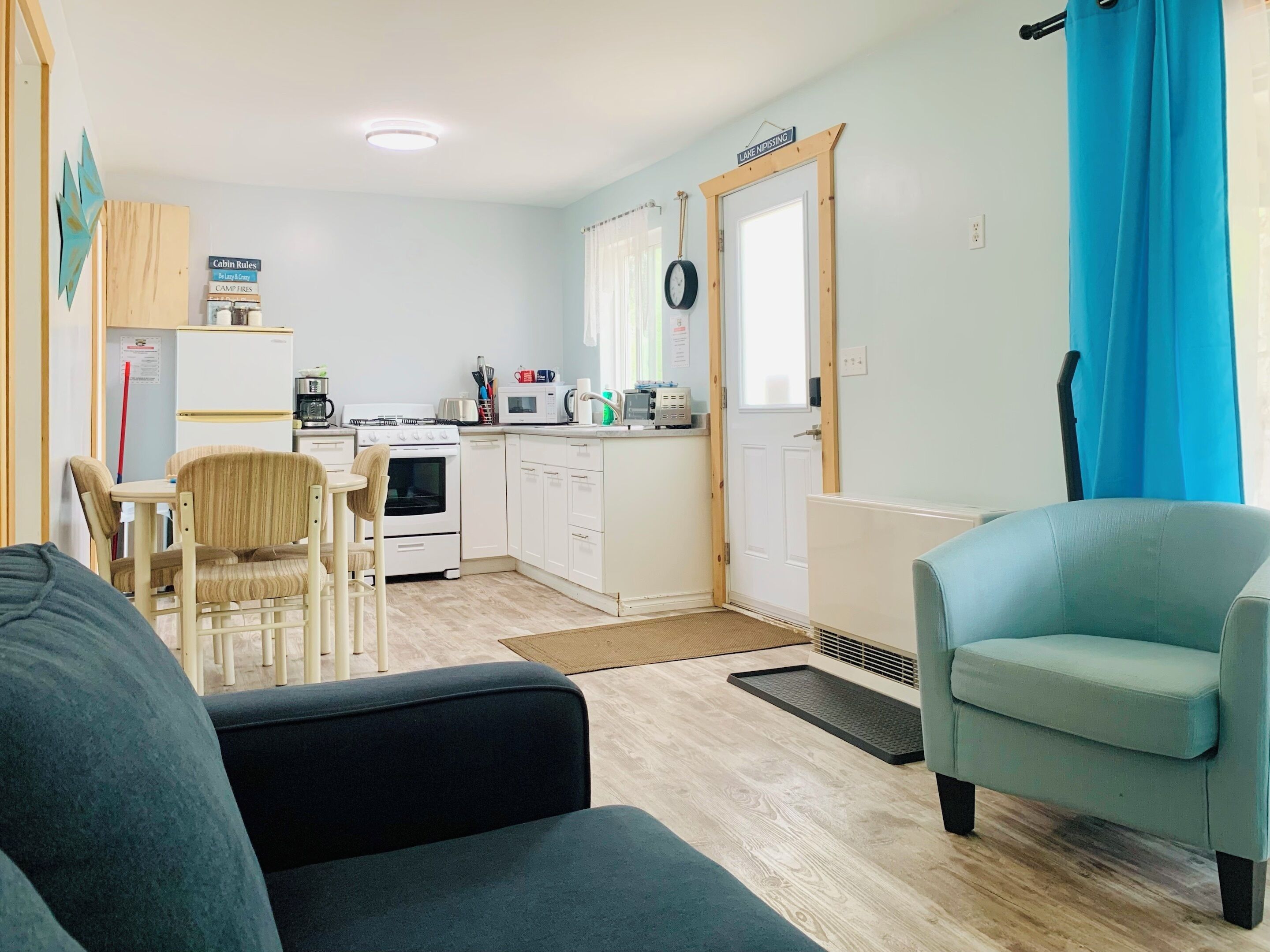 Un espacio habitable compacto con kitchenette, zona de comedor y sala de estar con sofá y sillones.