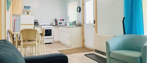 Un espacio habitable compacto con kitchenette, zona de comedor y sala de estar con sofá y sillones.