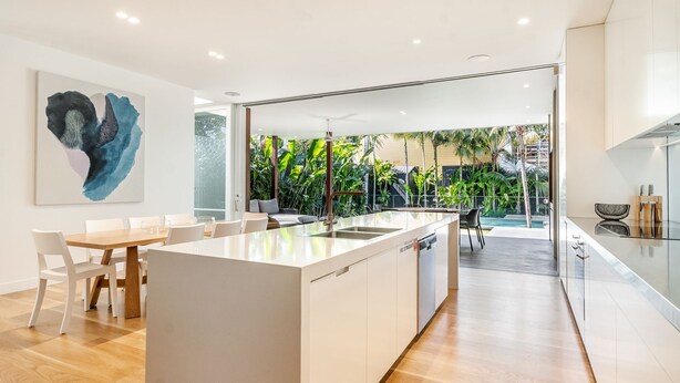 A modern kitchen with a central island, white cabinetry, and a view of a lush garden.