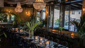 A restaurant interior with tables set for dining, large windows, and hanging crystal chandeliers.