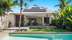 A modern house with a swimming pool, a covered patio, and lush greenery.