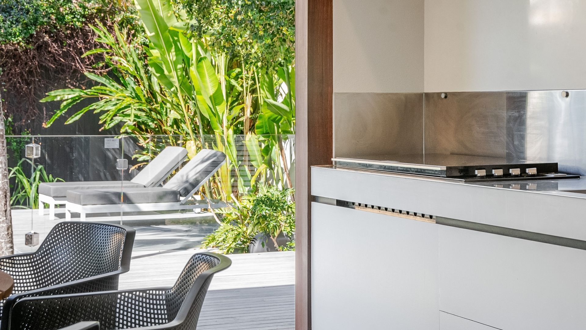 A modern outdoor kitchen with a gas stove, a white countertop, and a glass enclosure.