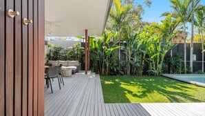 A wooden deck with outdoor furniture, a pool, and lush tropical plants.