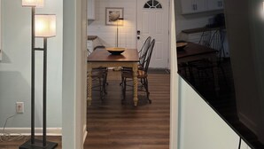 A dining area with a wooden table and chairs, a floor lamp, and a ceiling light fixture.