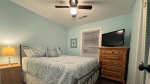 A bedroom with a bed, a nightstand, a dresser, a television, a ceiling fan, and a window with blinds.