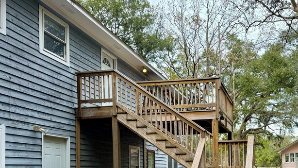 A two-story wooden house with a wooden staircase leading to a deck.