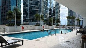 Una piscina con sillas de descanso, rodeada de edificios altos y palmeras.