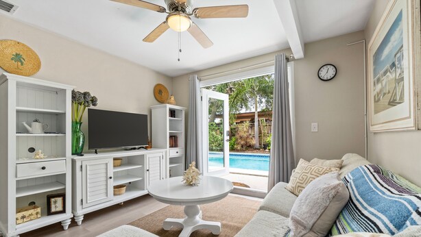 A living room with a TV, white cabinets, a ceiling fan, and a view of a swimming pool. - Discover Your Ideal Retreat in Fort Lauderdale (Fort Lauderdale)
