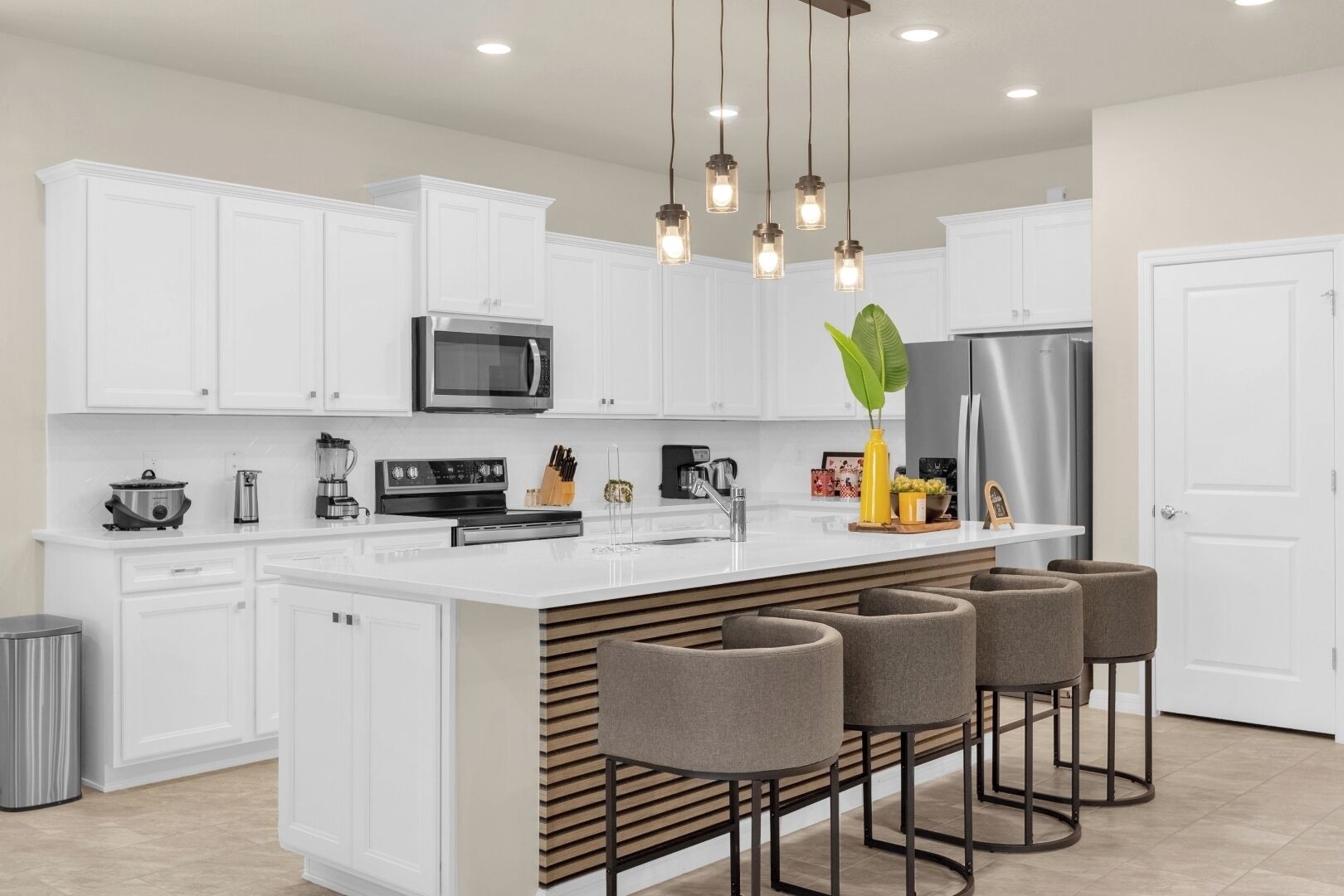 A modern kitchen with white cabinetry, stainless steel appliances, a central island with bar stools, and pendant lighting.