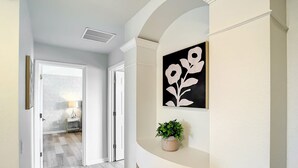 Un couloir au design moderne, agrémenté d’un mur orné d’un motif géométrique, d’une plante en pot et d’une œuvre d’art florale en noir et blanc.