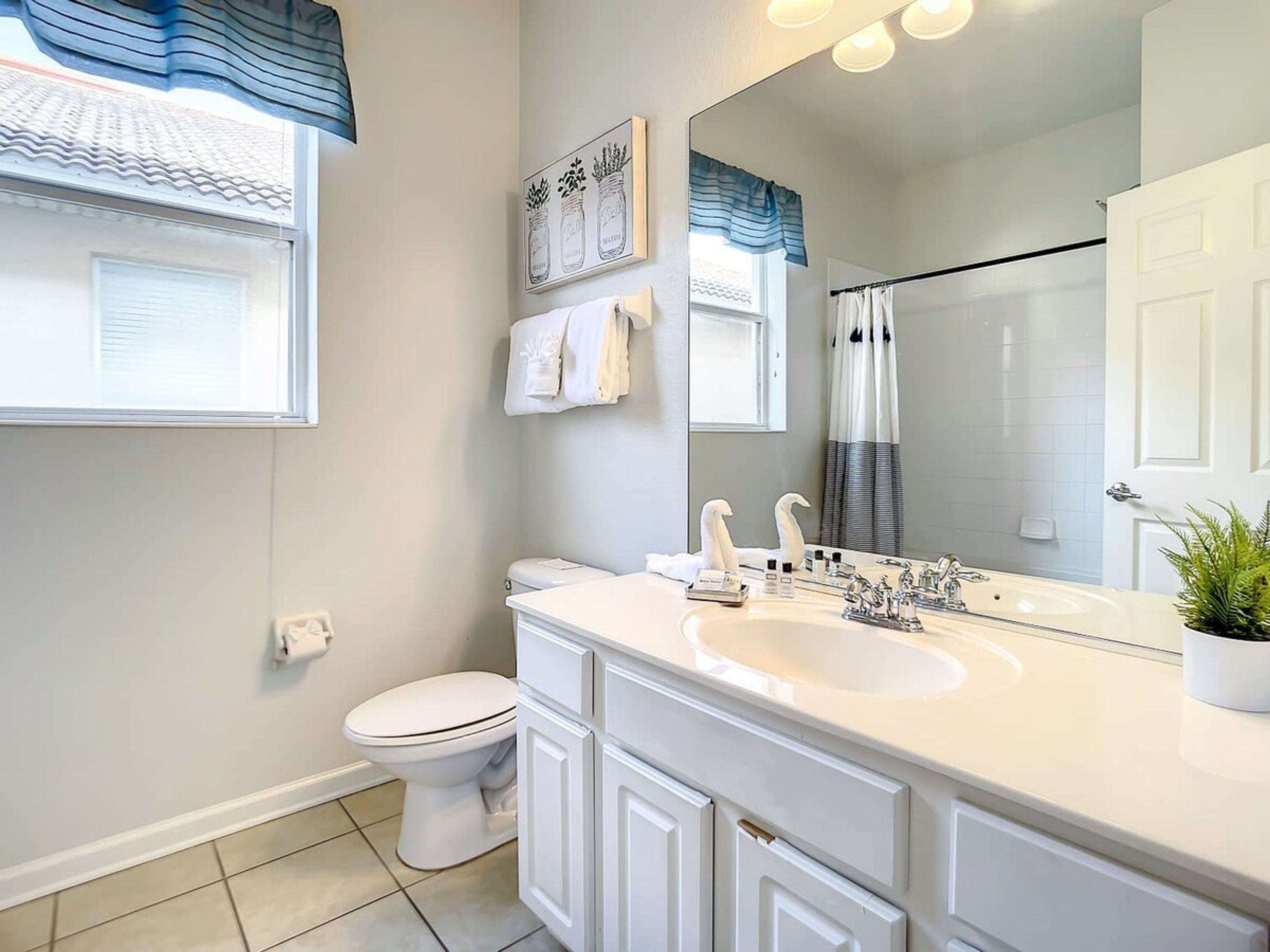 A modern bathroom with a white sink, vanity, and toilet. There is a large mirror above the sink and a shower area with a glass door.