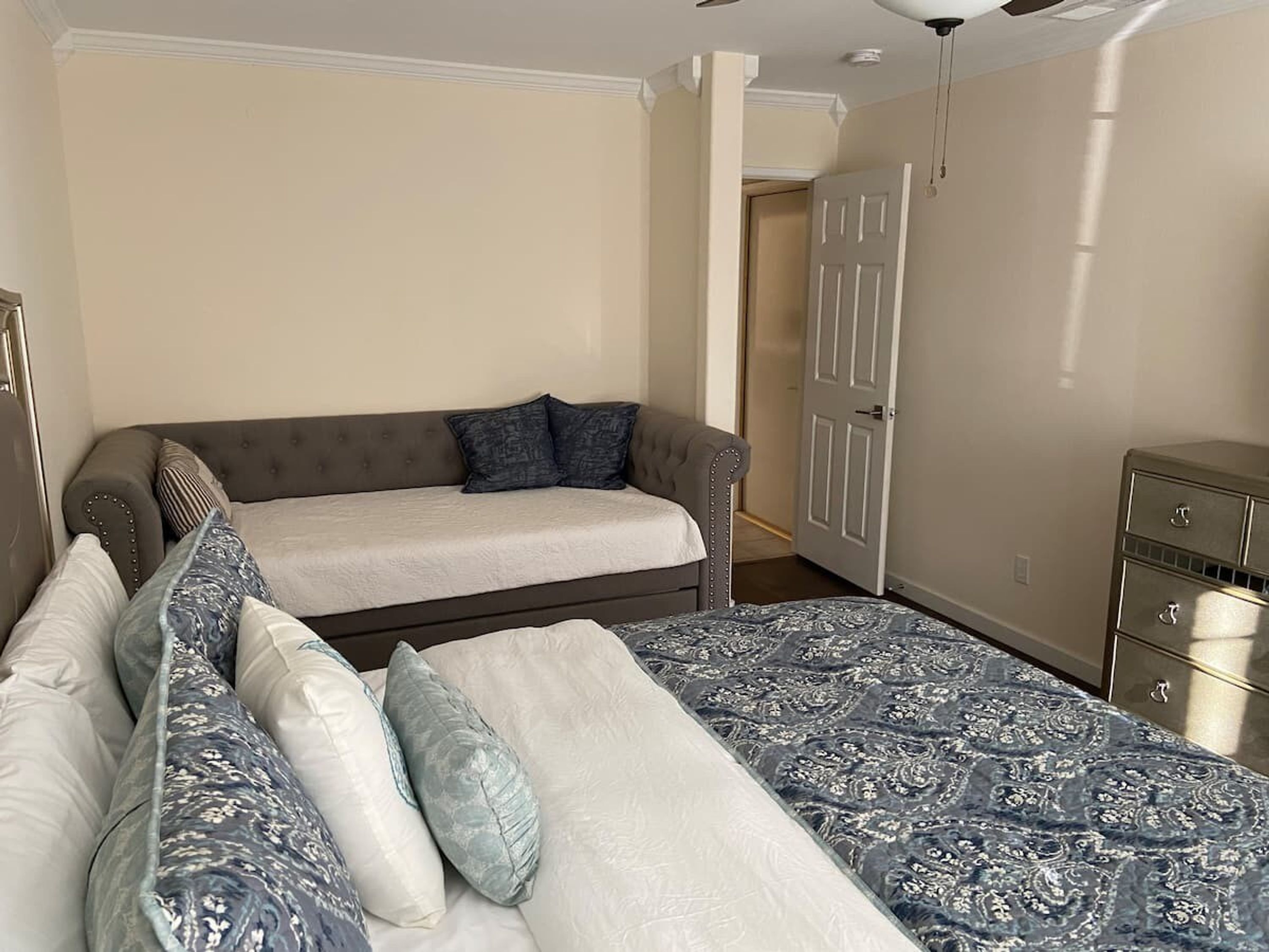 A bedroom with a bed, a sofa, a dresser, and a door leading to another room.