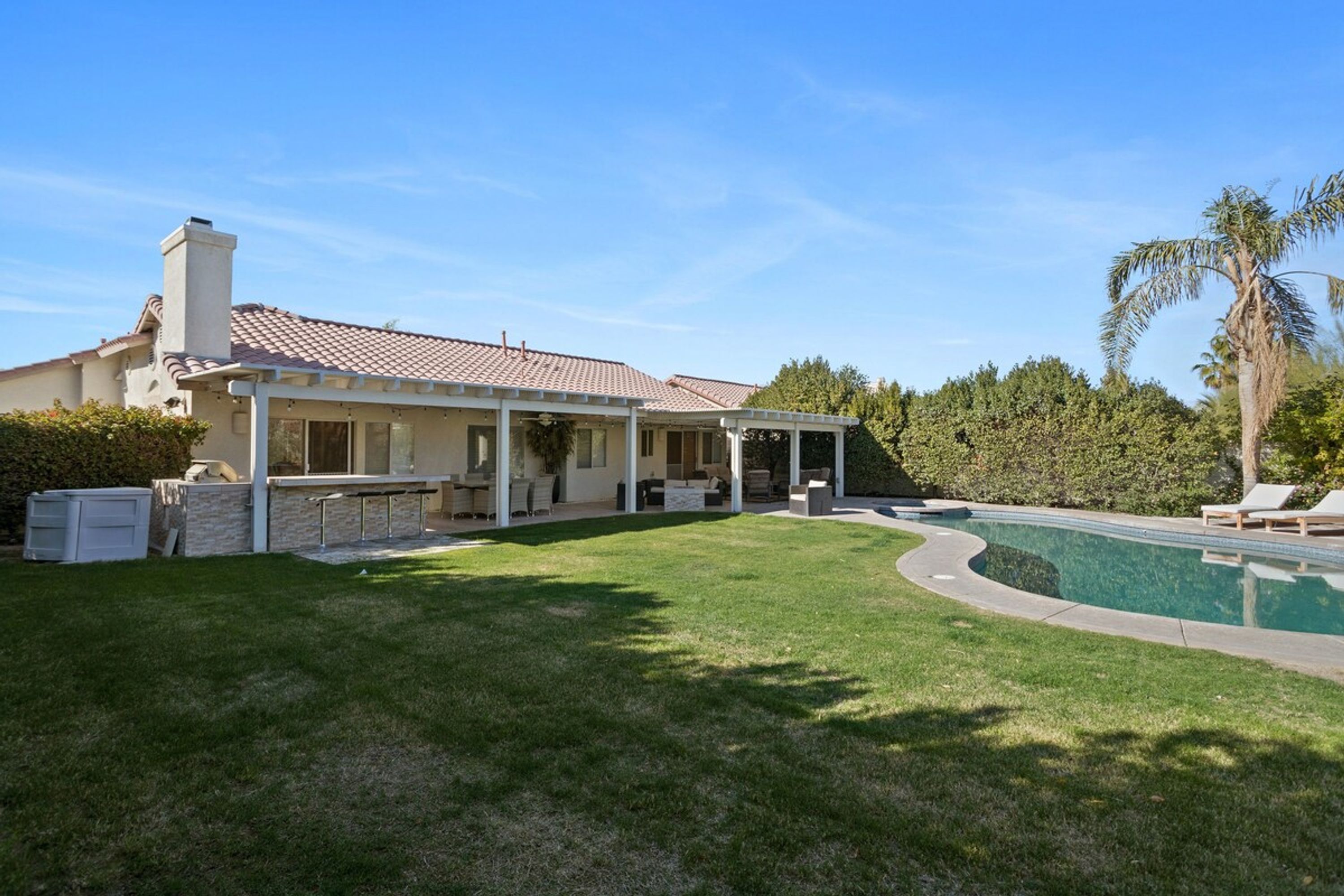 Una casa con piscina, un patio cubierto y un césped bien cuidado.
