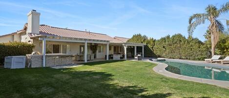 Una casa con piscina, un patio cubierto y un césped bien cuidado.
