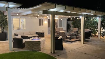 An outdoor patio with a covered seating area, a fire pit, and string lights.