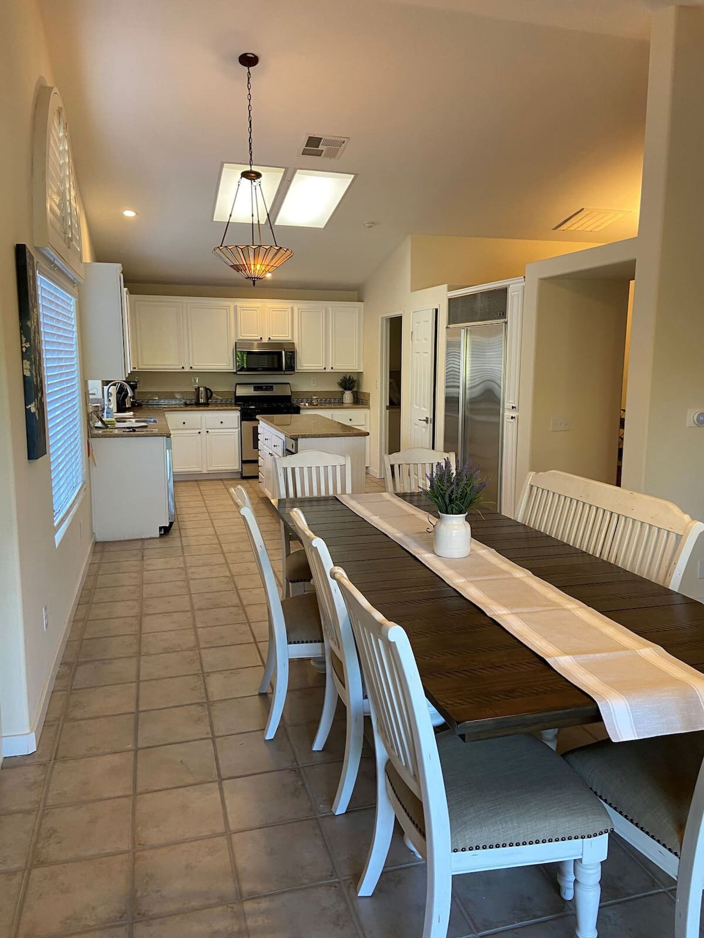 A modern kitchen with white cabinets, a central island, and a dining area with a long table and white chairs.