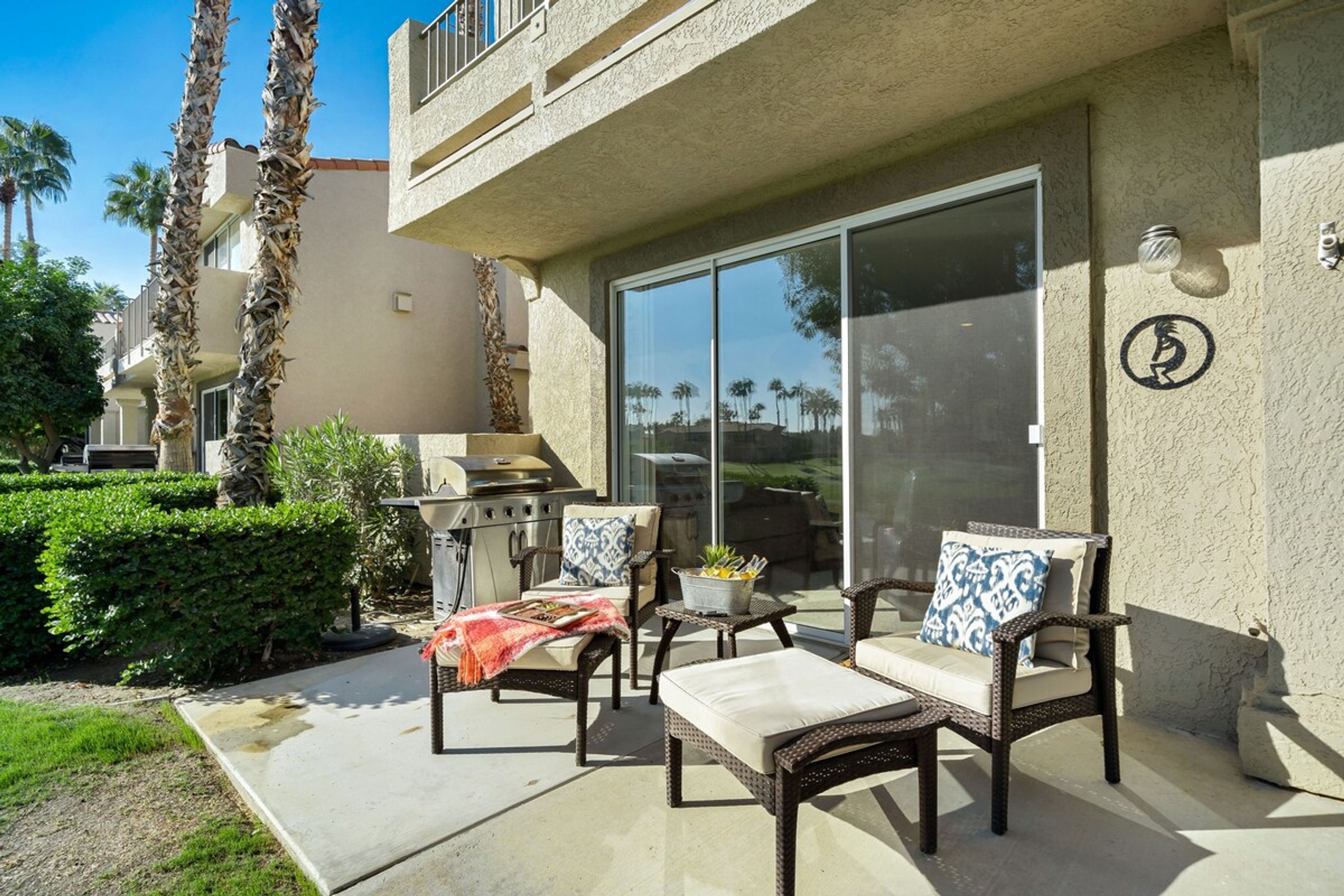 An outdoor patio with wicker furniture, a grill, and a sliding glass door leading to a balcony.