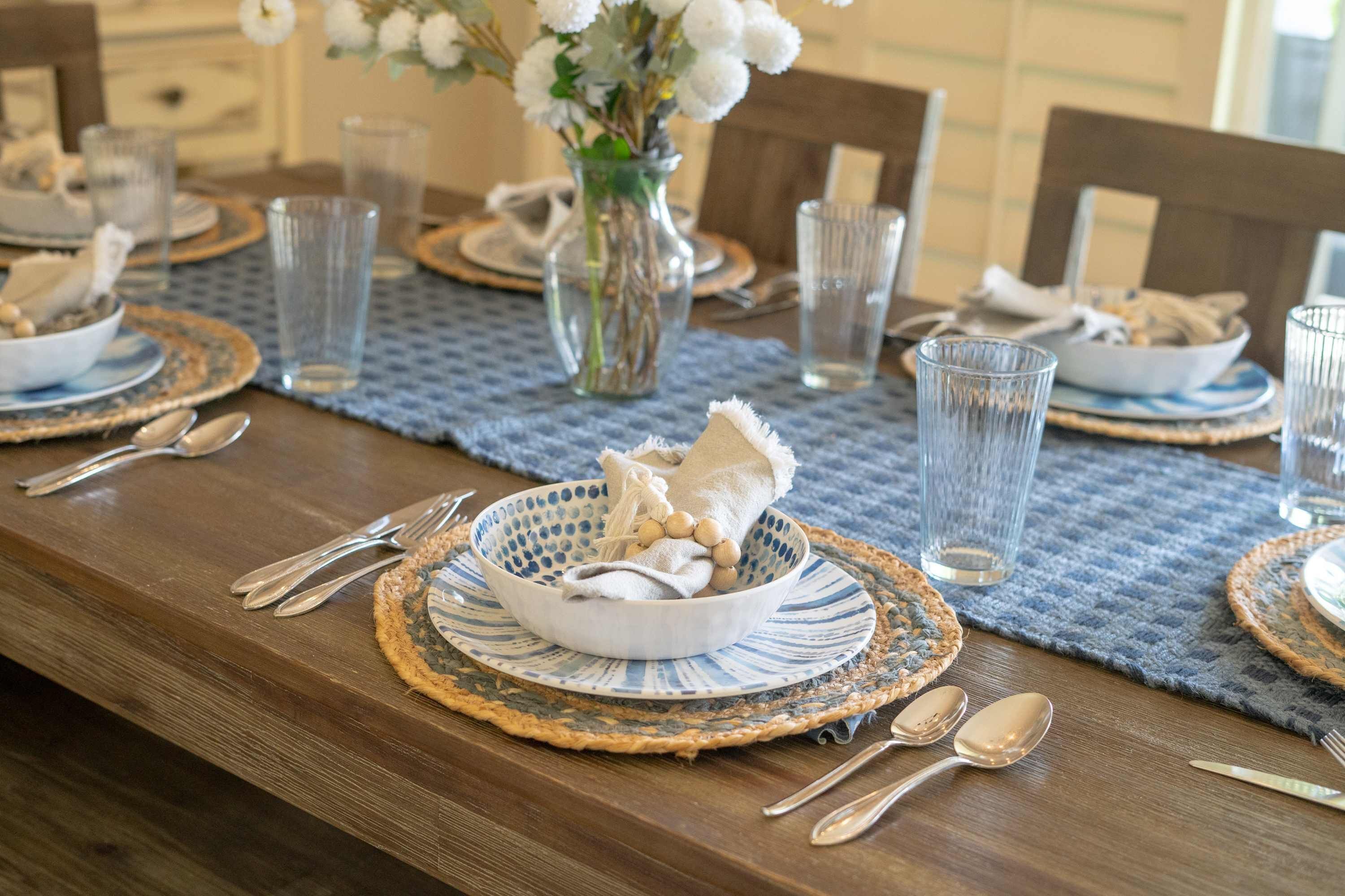 A dining table set with plates, bowls, cutlery, and glasses, with a vase of flowers in the center.