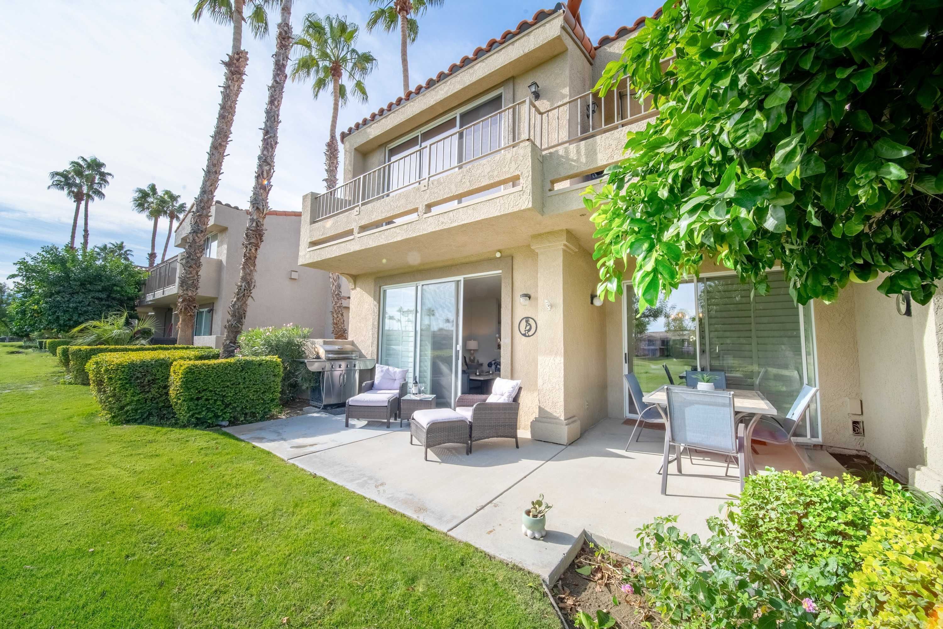 A two-story house with a patio, outdoor furniture, and a view of the neighborhood.