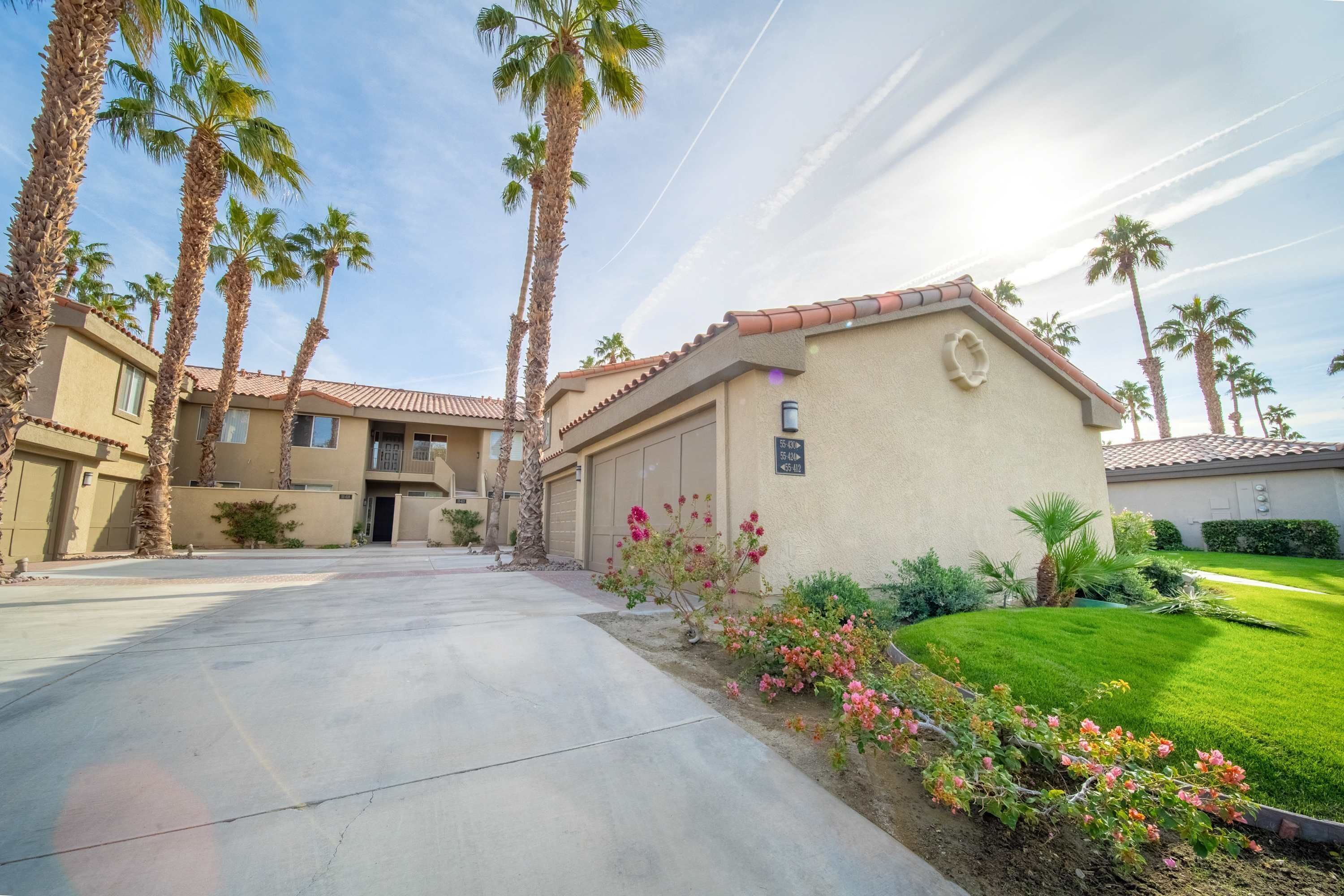 A residential area with a house featuring a tiled roof, a driveway, and a well-maintained lawn with pink flowers.