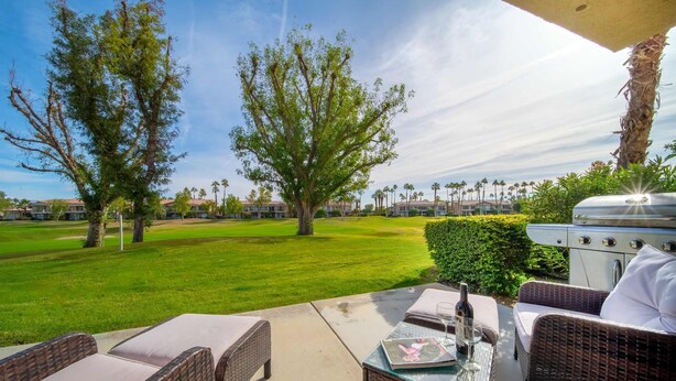 Un patio al aire libre con mobiliario de mimbre, una parrilla y vistas a un campo de golf.