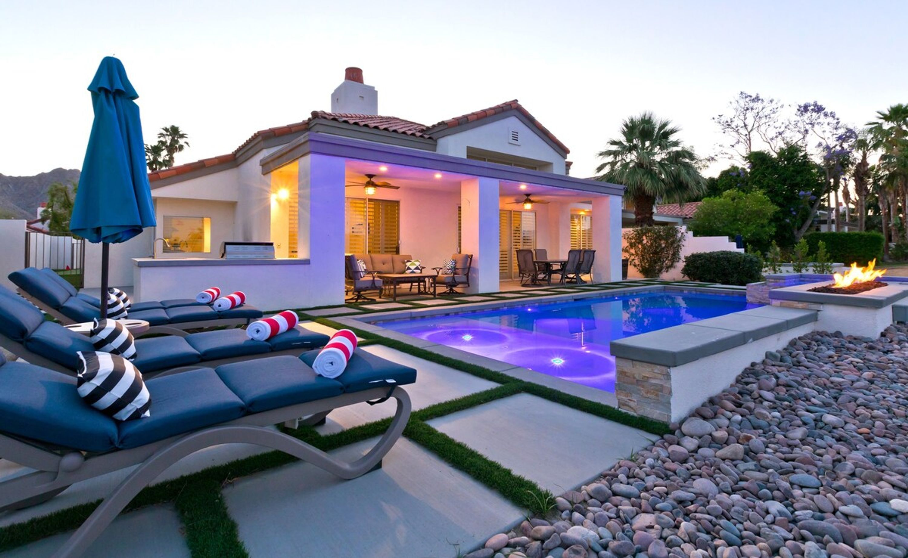 A poolside area with lounge chairs, a dining area, and a house with a patio.