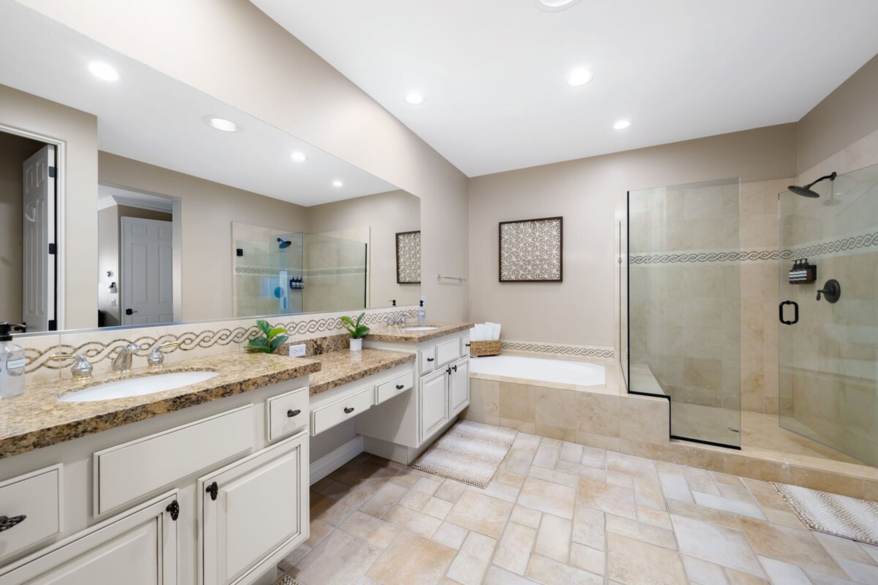 Un baño moderno con un espejo grande, dos lavamanos, una bañera y una ducha con mampara de vidrio.