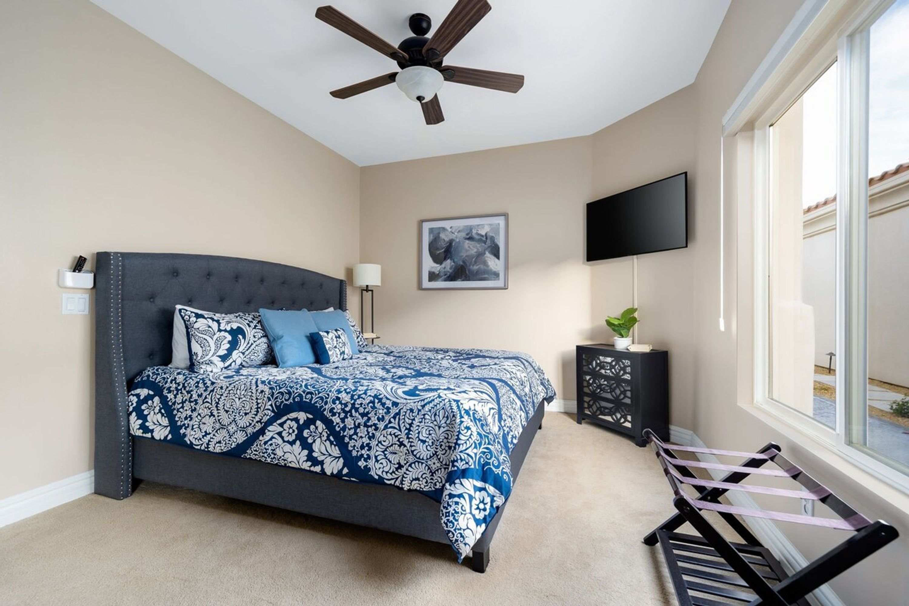 A bedroom with a bed, a ceiling fan, a TV, and a window.