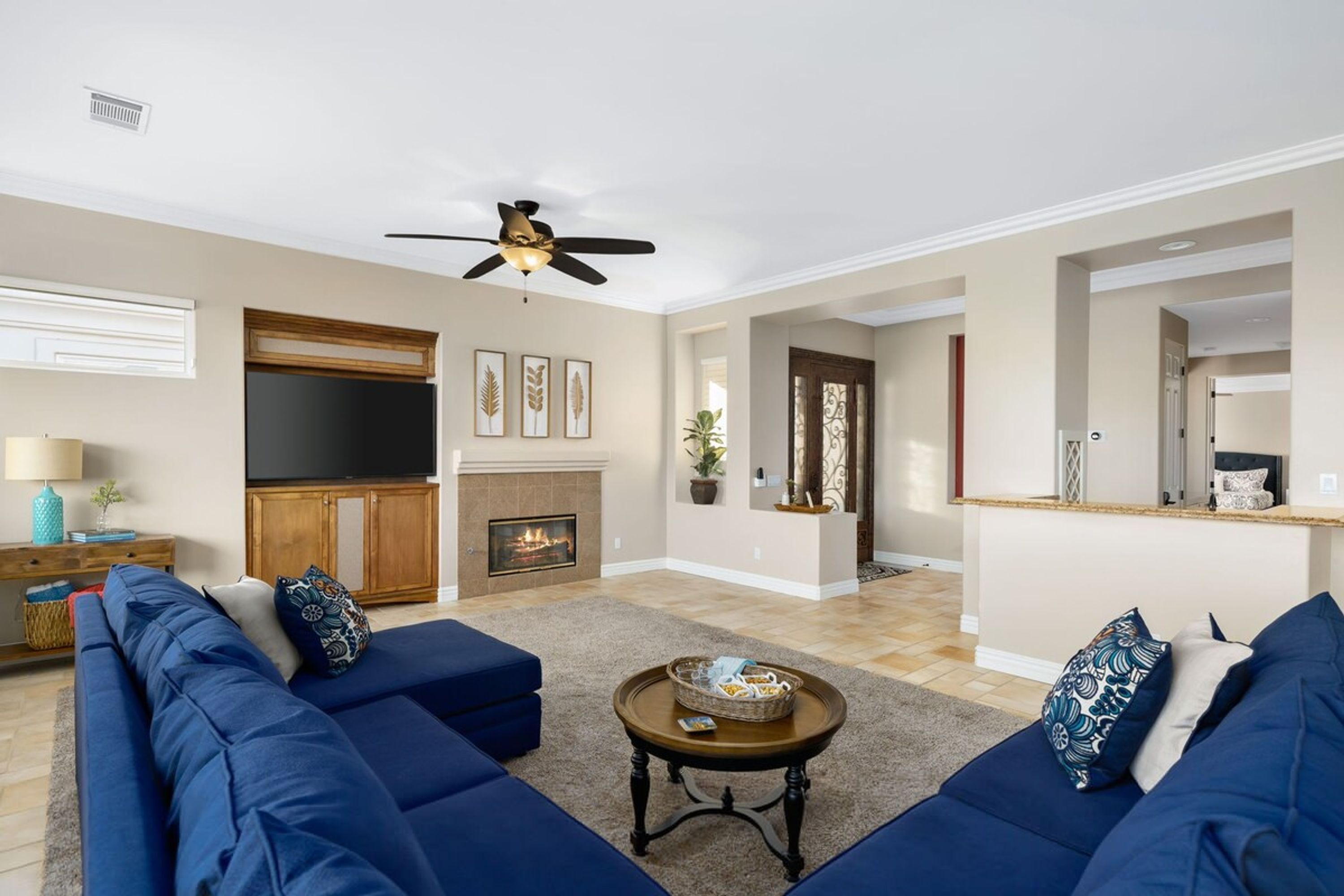 A living room with a fireplace, blue sofas, a coffee table, and a ceiling fan.