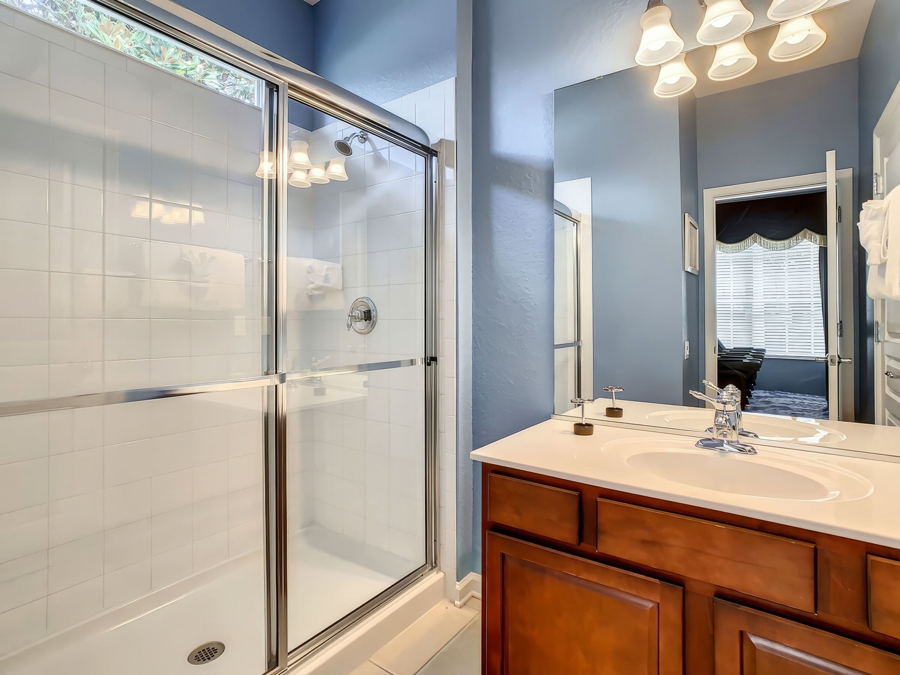 A modern bathroom with a glass-enclosed shower, a large mirror, and a vanity with a sink.