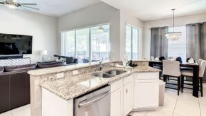 A modern kitchen with granite countertops, stainless steel appliances, and a dining area with a chandelier. - Ultimate Adventure Villa Top Rated 5 Star Disney More (Kissimmee)