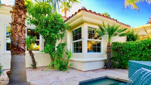 A pool area with a water feature, surrounded by palm trees and a building with large windows.