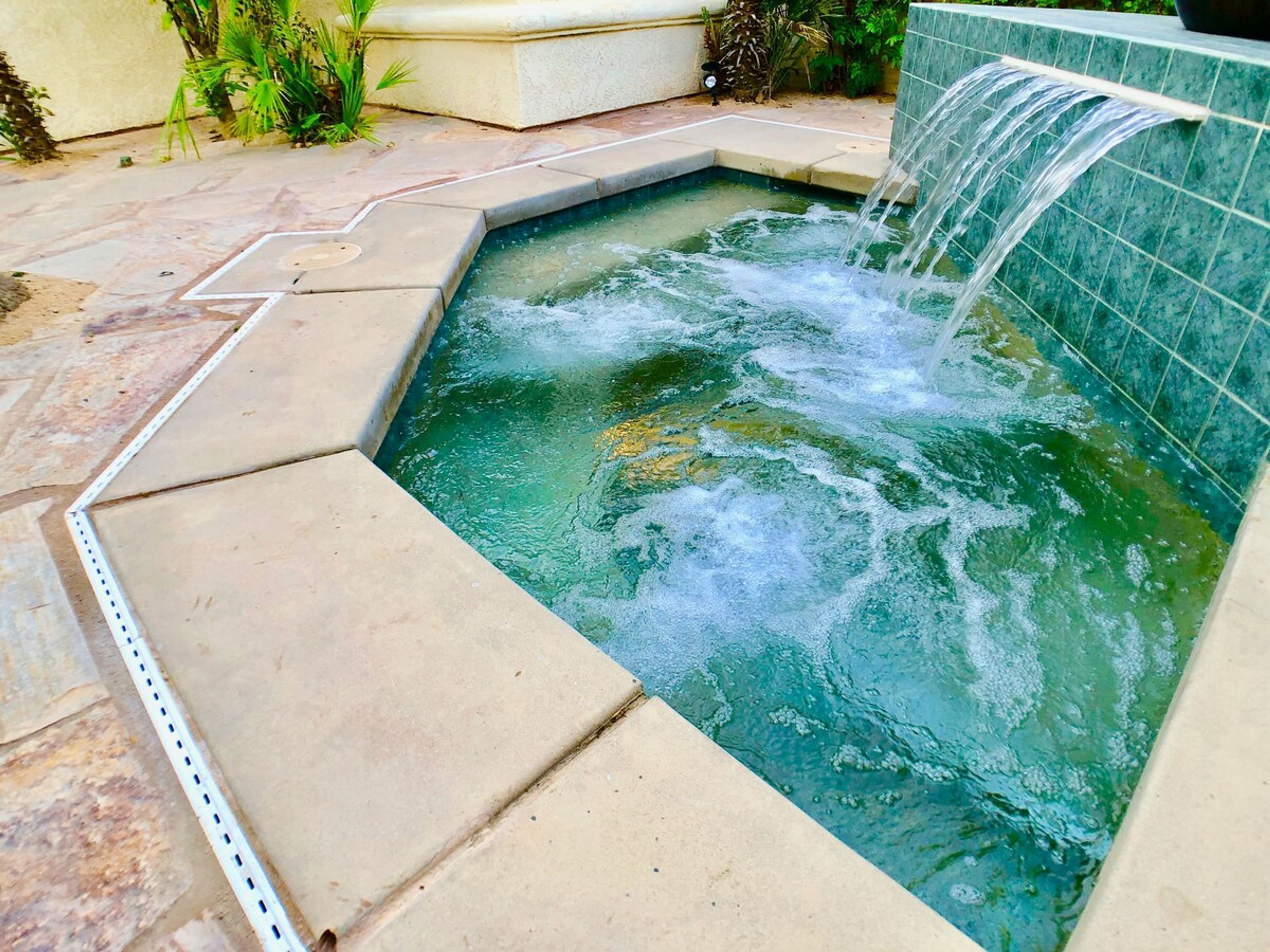 A rectangular hot tub with a waterfall feature, surrounded by a tiled patio.