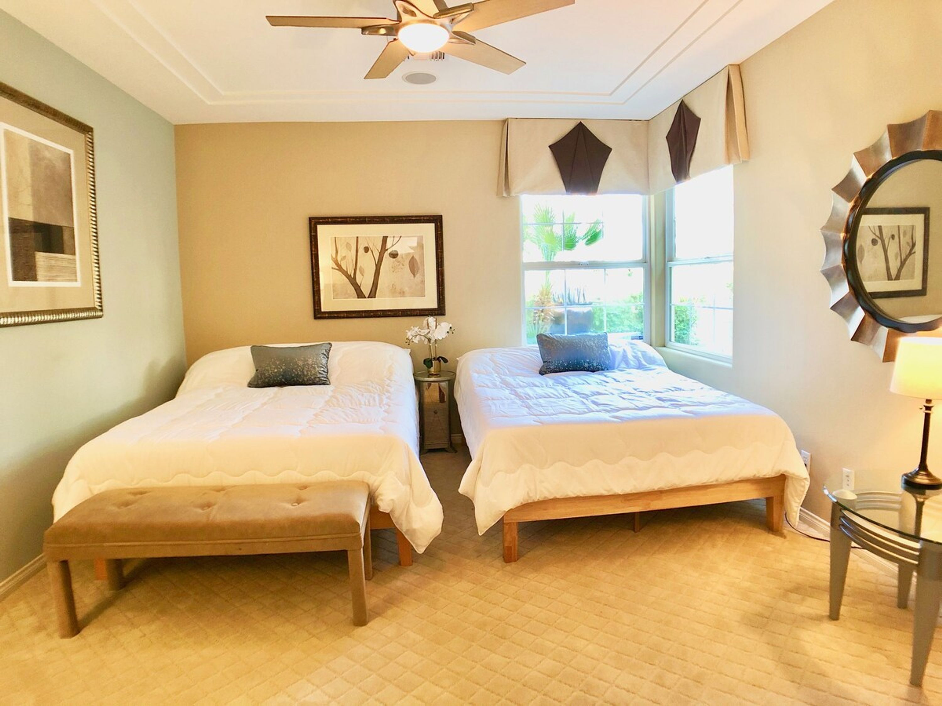 A bedroom with two beds, a ceiling fan, a window with curtains, and a framed picture on the wall.