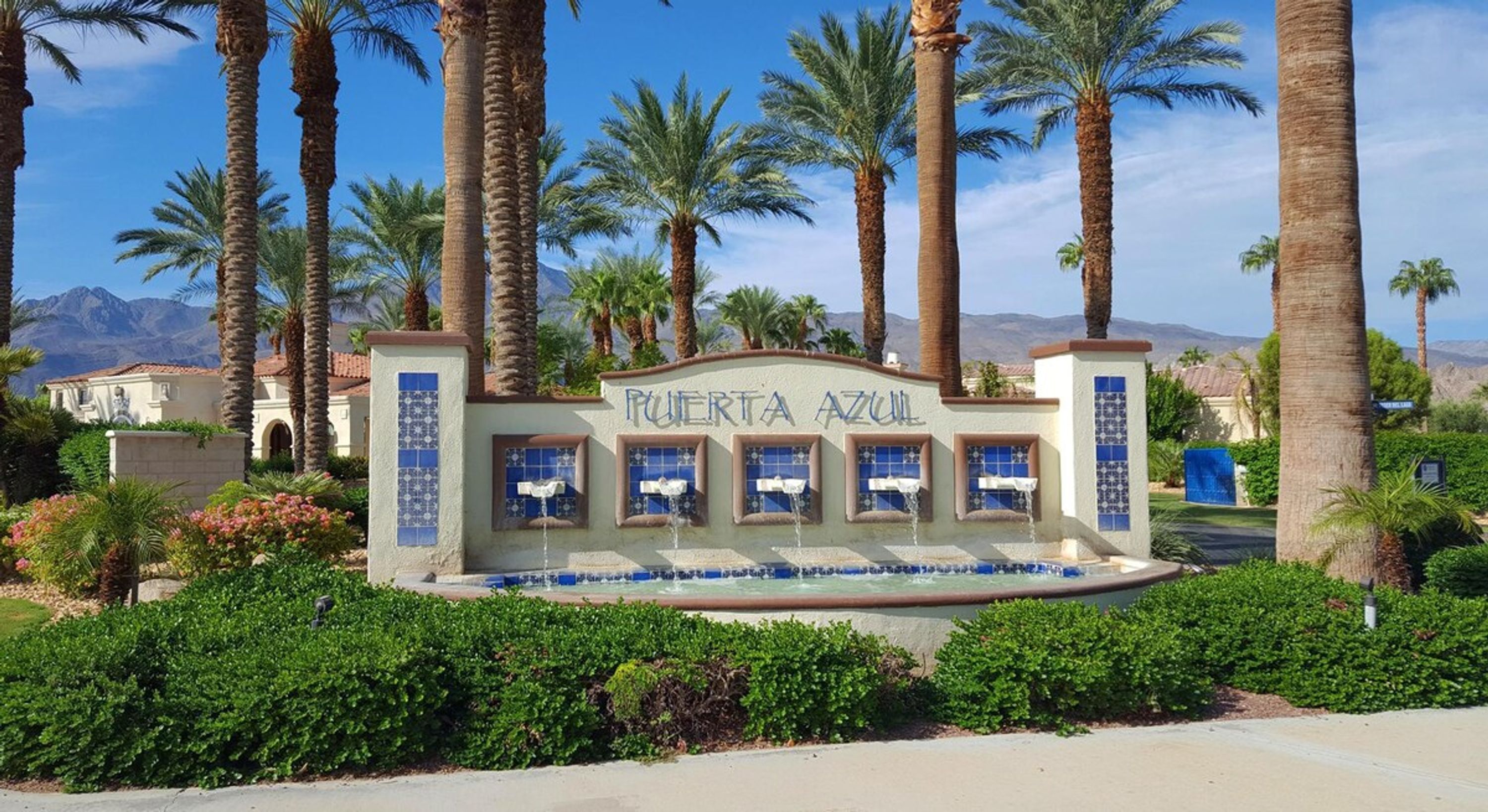 Señal con la inscripción 'PUERTA AZUL' que indica la entrada a un hotel, rodeado de palmeras y un paisaje montañoso.