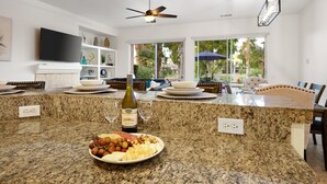 Una cocina con encimeras de granito, un comedor con mesa y sillas, un ventilador de techo y un ventanal con vistas al exterior.