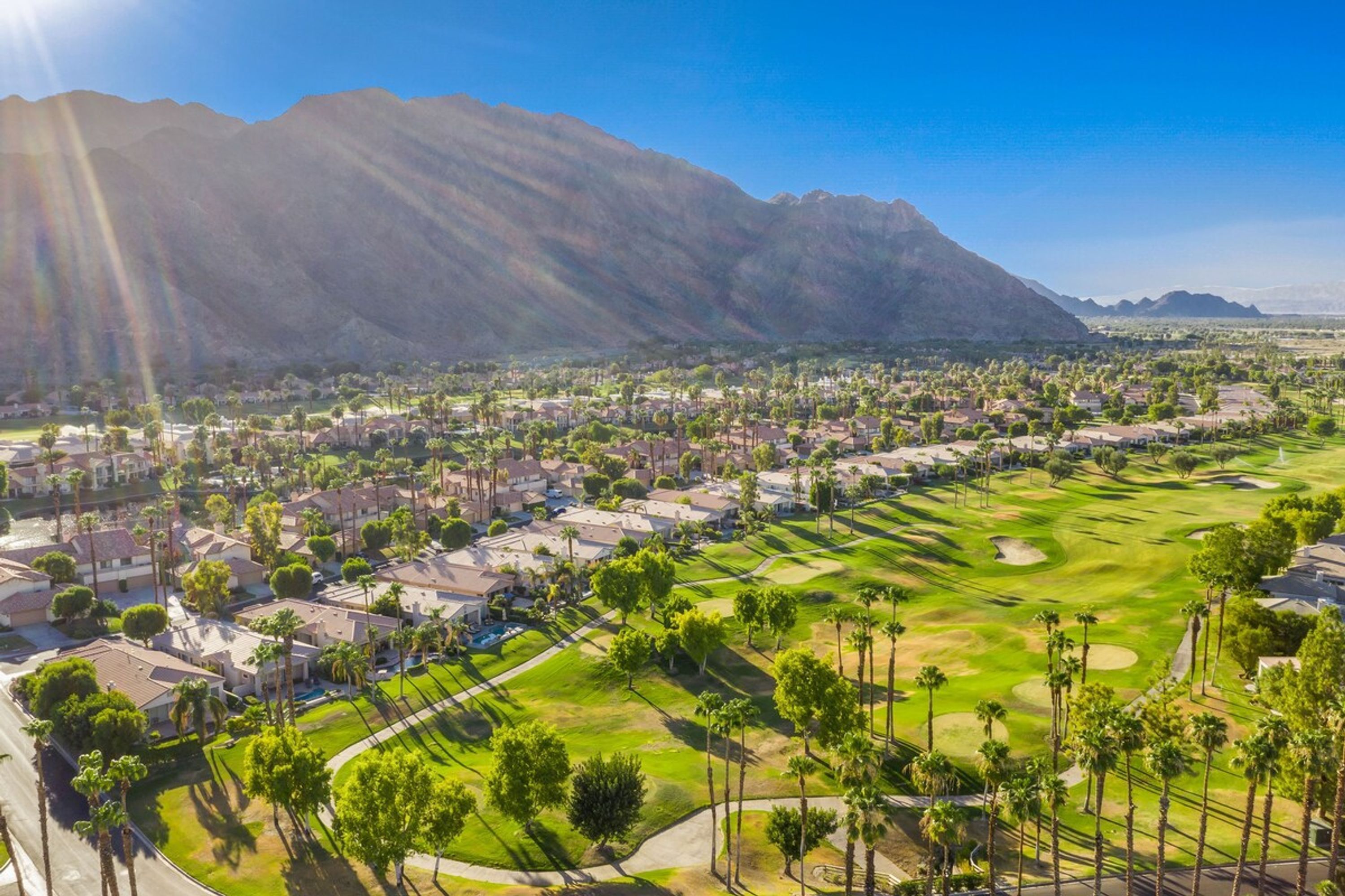 Zona residencial con casas, un campo de golf y montañas al fondo.