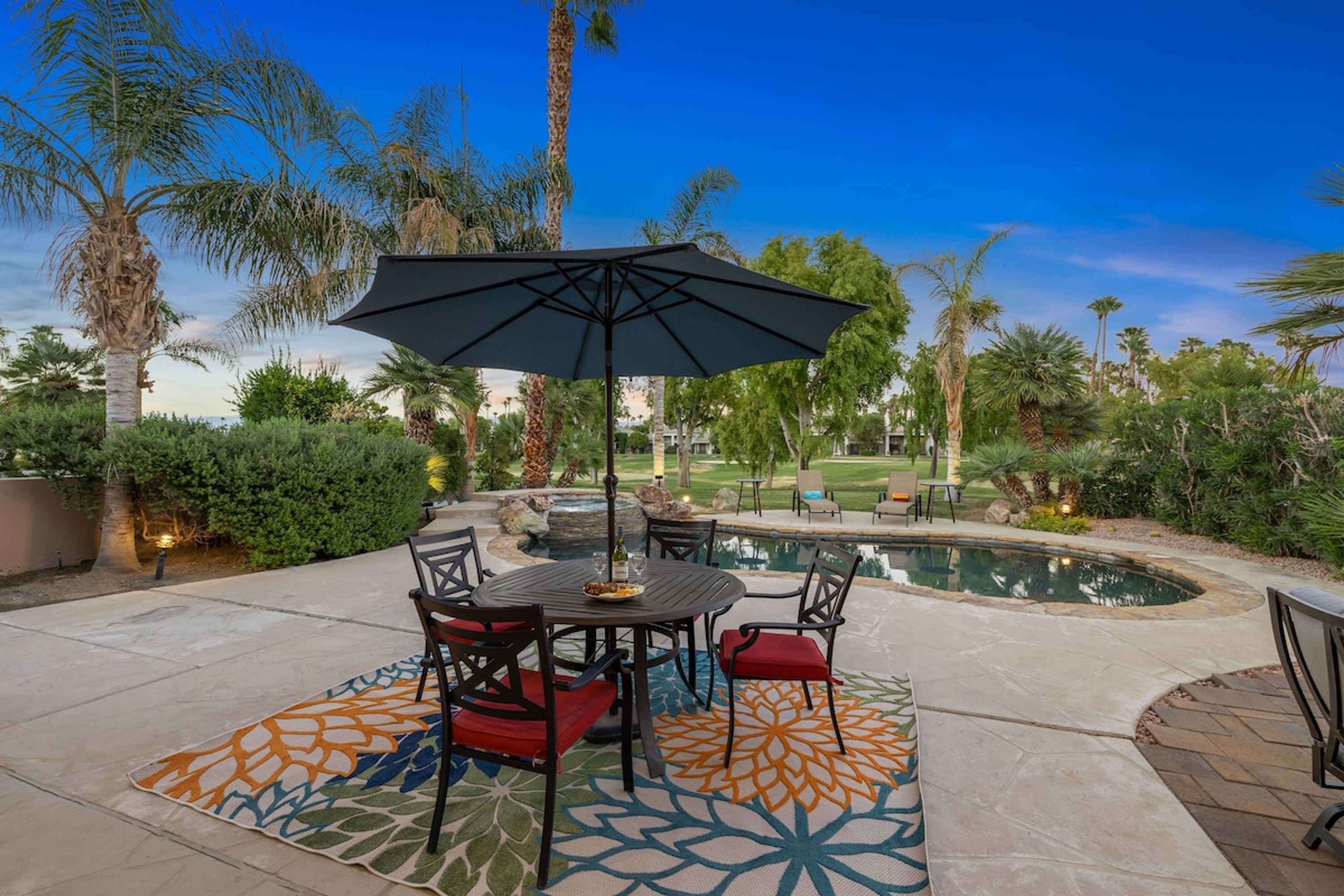 An outdoor patio with a pool, surrounded by palm trees and a well-maintained lawn.