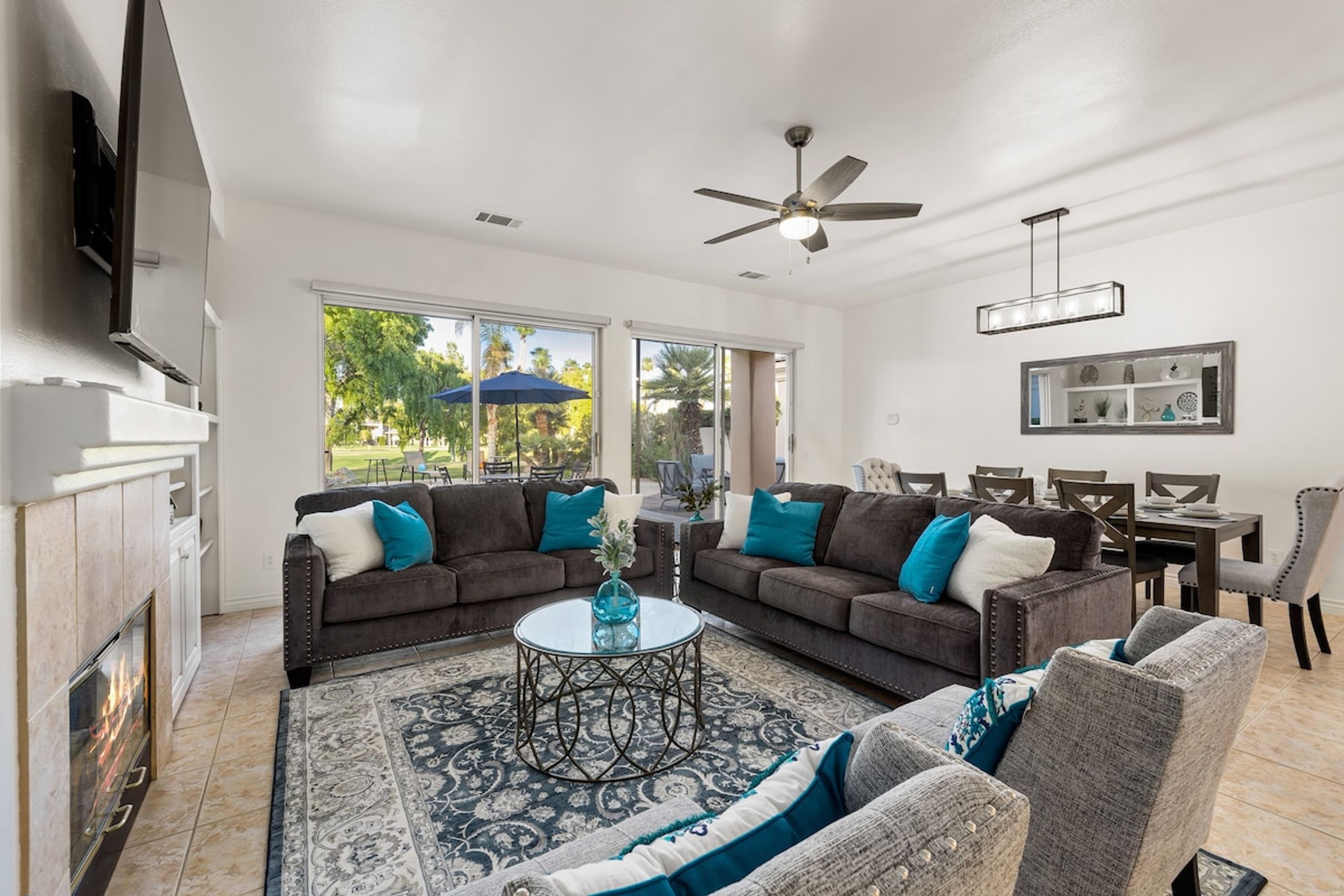 A spacious living room with a fireplace, a ceiling fan, and a dining area with a table and chairs.
