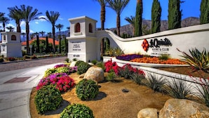 Entrada de un complejo turístico con un letrero de 'La Quinta' que muestra un club de tenis, tiendas y un centro turístico y club.